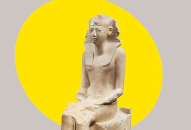 An ancient Egyptian seated statue of Hatshepsut in limestone, with a bright yellow ovular spotlight shape behind the figure in the background
