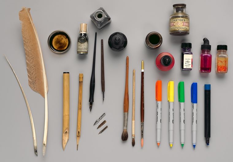 A neat arrangement of inks, pens, and feather quills placed on a grey tabletop.