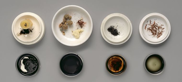 A neat arrangement of liquid inks in open containers below plates of the materials they are ground from.